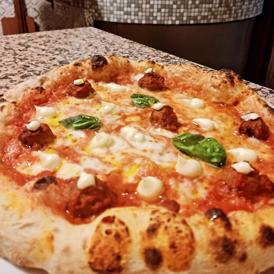 Pizza con polpette e fior di latte davanti al forno a mosaico della pizzeria